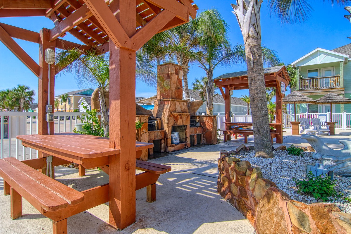 Gather around your private outdoor oasis featuring a stone fireplace, tiki bar, and tropical palm trees for perfect beach house entertaining.