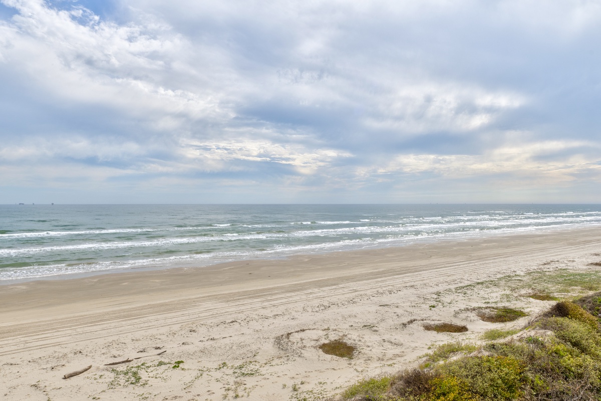 Pristine sandy beach stretches along the coastline with gentle waves and dramatic cloudy skies above.