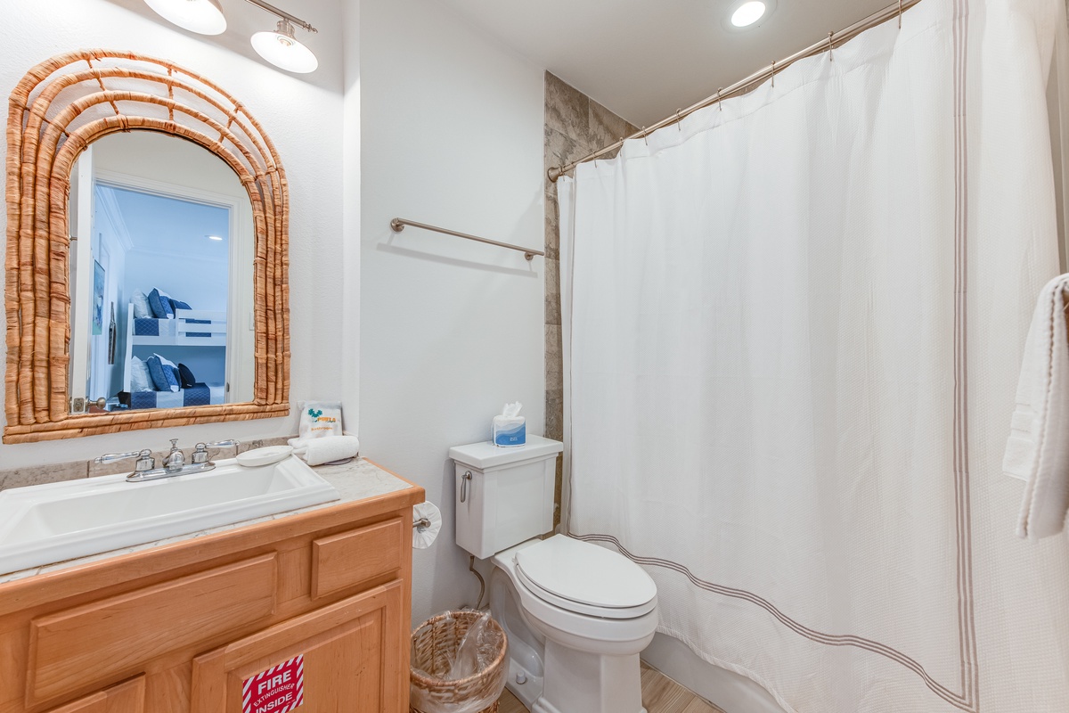 Refresh in your private bathroom featuring a relaxing tub-shower combo, elegant wicker mirror, and thoughtful amenities for your comfort.