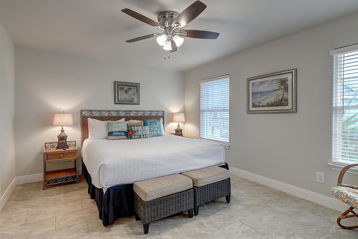 Relax in your coastal-themed bedroom with crisp linens, ceiling fan, and cheerful ocean artwork creating the perfect vacation retreat.