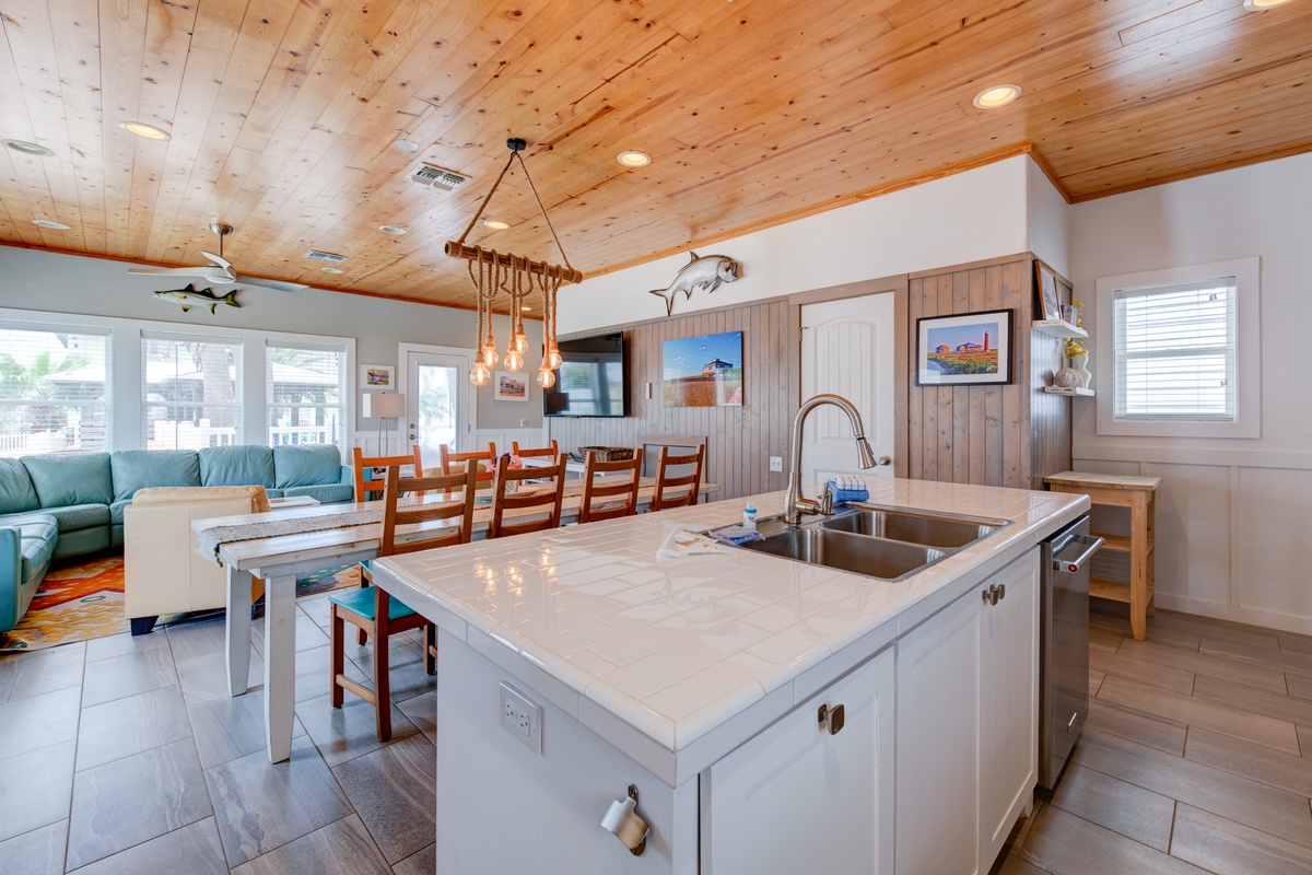 Your open-concept kitchen flows seamlessly into the dining area, where warm wood ceilings and coastal touches create the perfect gathering space.