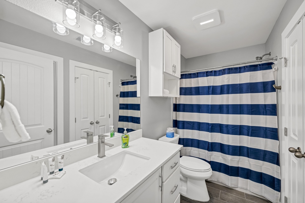 Step into your crisp, modern bathroom with bright vanity lighting and nautical-striped shower curtain creating a fresh, coastal vibe.