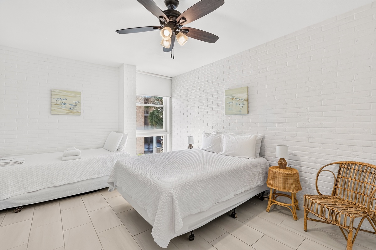 Unwind in your bright, breezy bedroom with fresh white linens and coastal touches. The ceiling fan keeps you cool while natural light streams in from your private window.