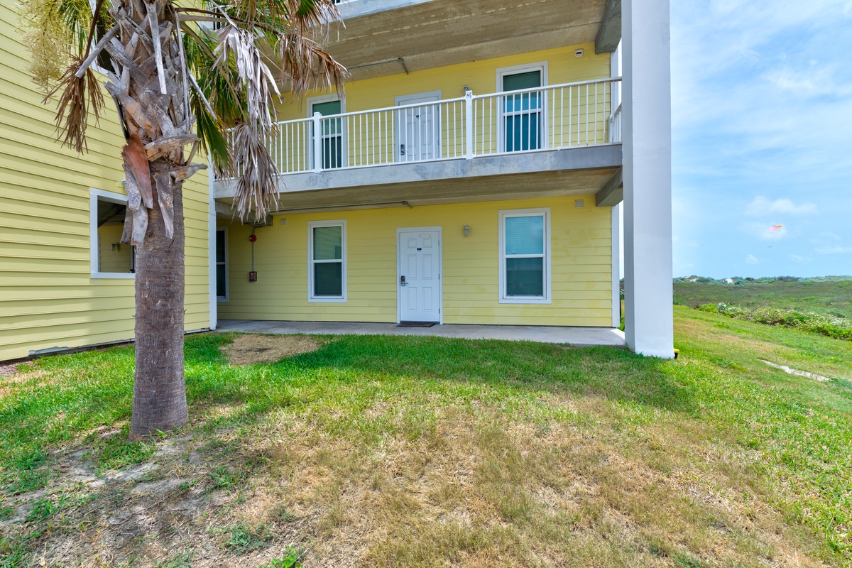This cheerful yellow coastal property features a welcoming design with a private patio and tropical palm trees. The open lawn and nearby natural landscape create a peaceful retreat setting for your beach getaway.