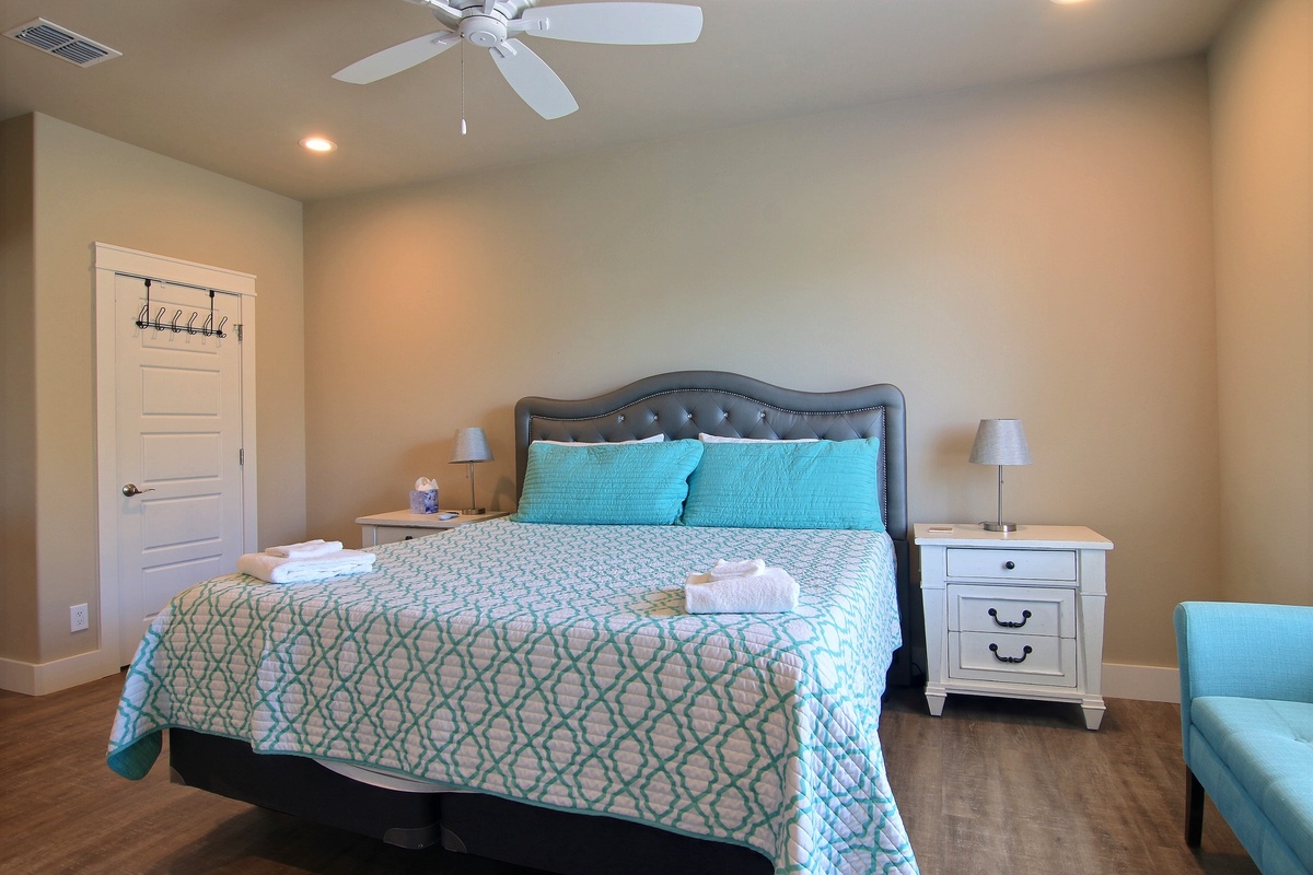 Sink into your cozy bedroom featuring a plush upholstered bed with fresh linens, bedside tables, and a relaxing ceiling fan overhead.