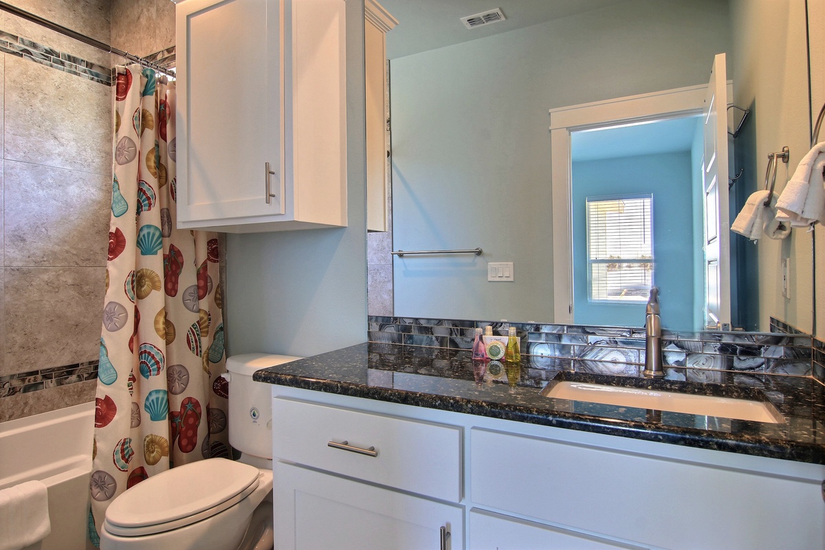 Your stylish bathroom features granite counters, white cabinetry, and a cheerful seashell-themed shower curtain that perfectly captures the coastal vibe.