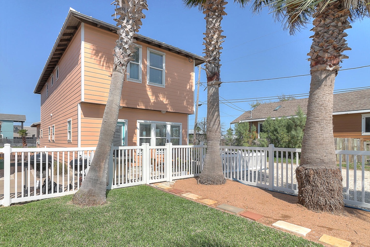 Charming coastal property featuring a bright orange exterior with palm trees and white picket fence in a peaceful residential neighborhood.