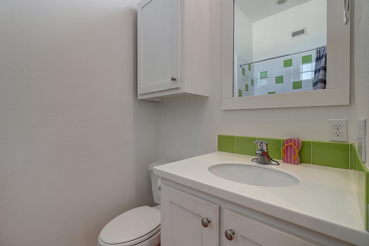 Your bright bathroom features vibrant green tile accents and thoughtful storage with crisp white cabinetry and countertops.
