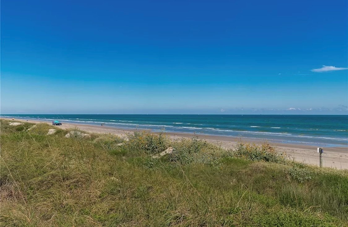 Pristine coastline with golden sand beach stretching beneath brilliant blue skies and rolling ocean waves.
