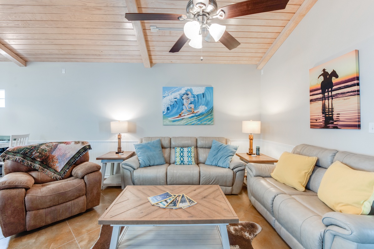 Sink into your spacious living room with comfortable seating for everyone, coastal artwork, and exposed beam ceilings creating the perfect gathering space.