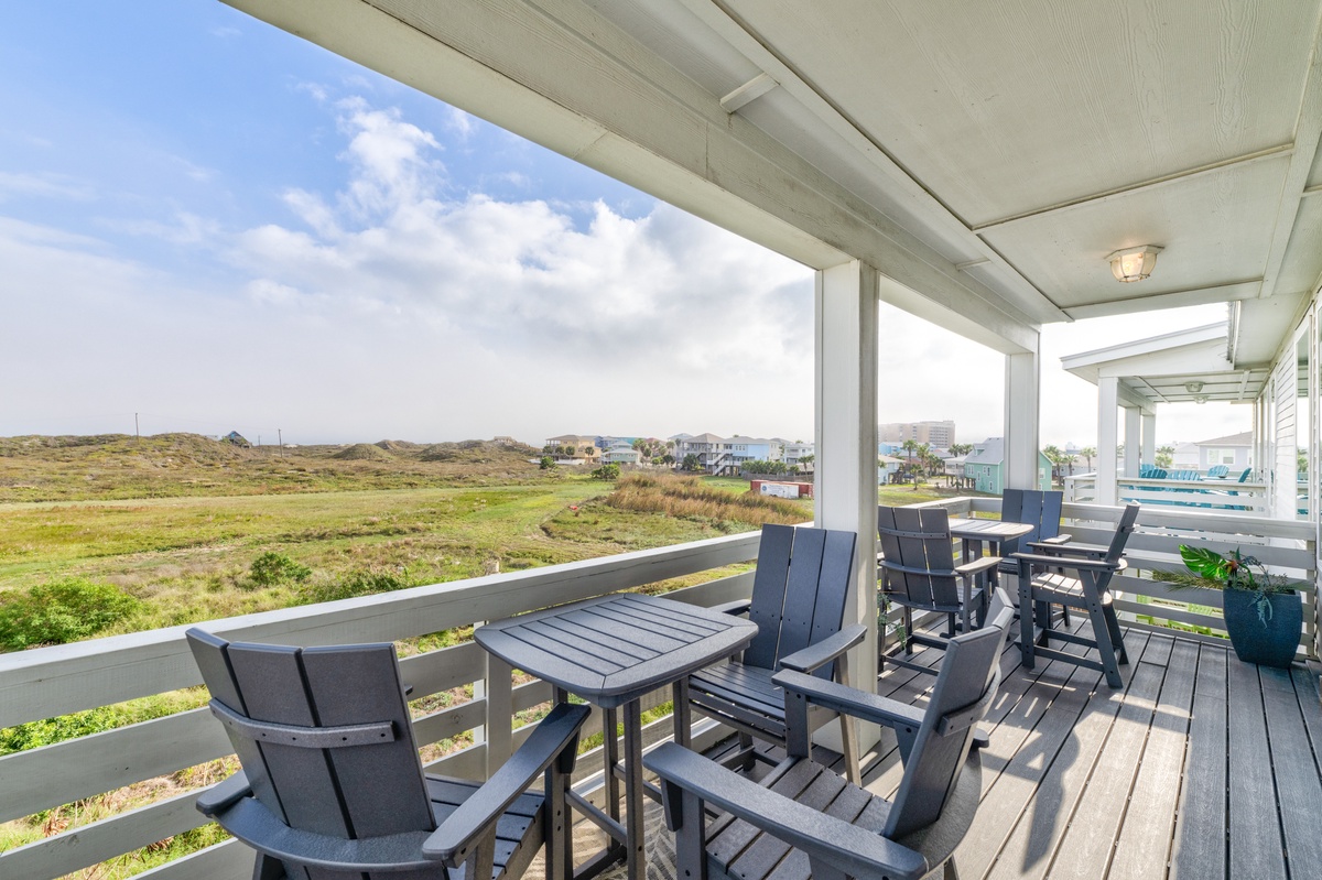 Relax on your covered balcony with comfortable seating while enjoying peaceful views of the natural landscape stretching toward distant homes.