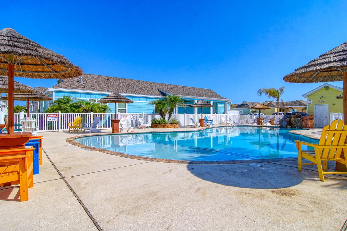 Sparkling pool surrounded by tropical thatched umbrellas and colorful beach furniture under brilliant blue skies at this coastal resort property.