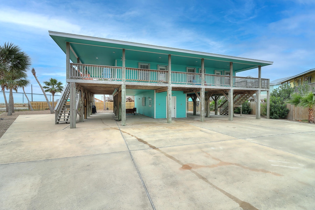 Charming beach house on stilts with turquoise exterior and covered parking beneath the elevated living space.