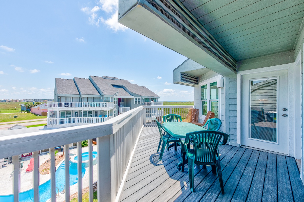 Step onto your private deck where turquoise chairs invite alfresco dining with stunning pool views and coastal scenery stretching beyond.