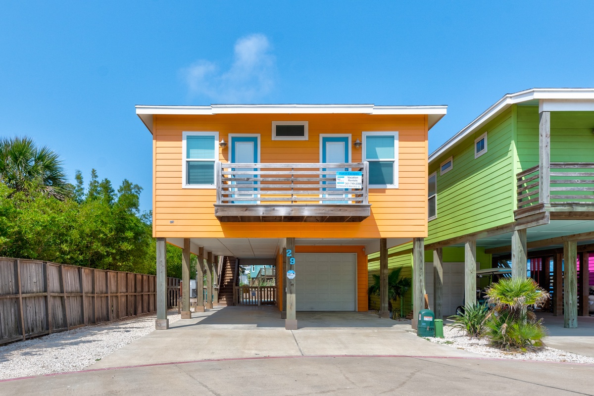 Vibrant orange beach house with covered parking and tropical landscaping in a colorful coastal neighborhood.