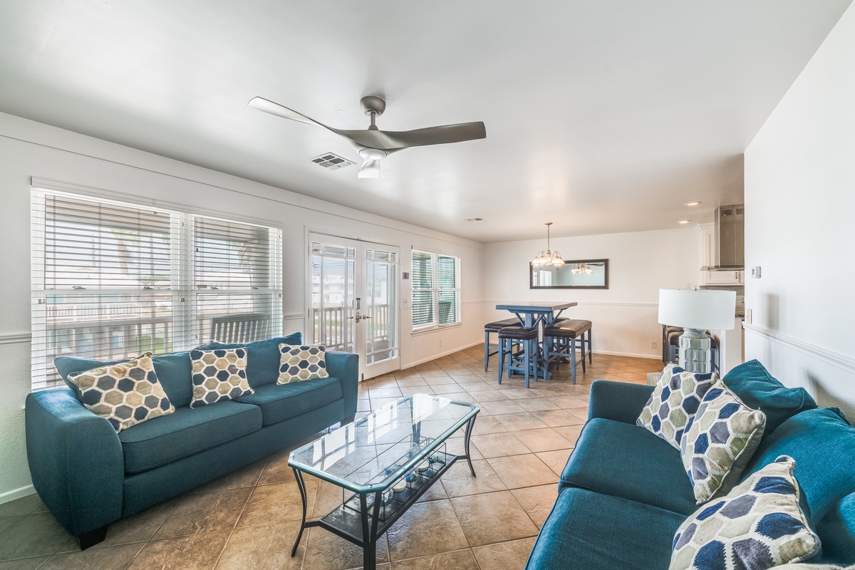 Relax in your spacious living area with plush teal sofas, natural light streaming through French doors to your private balcony.