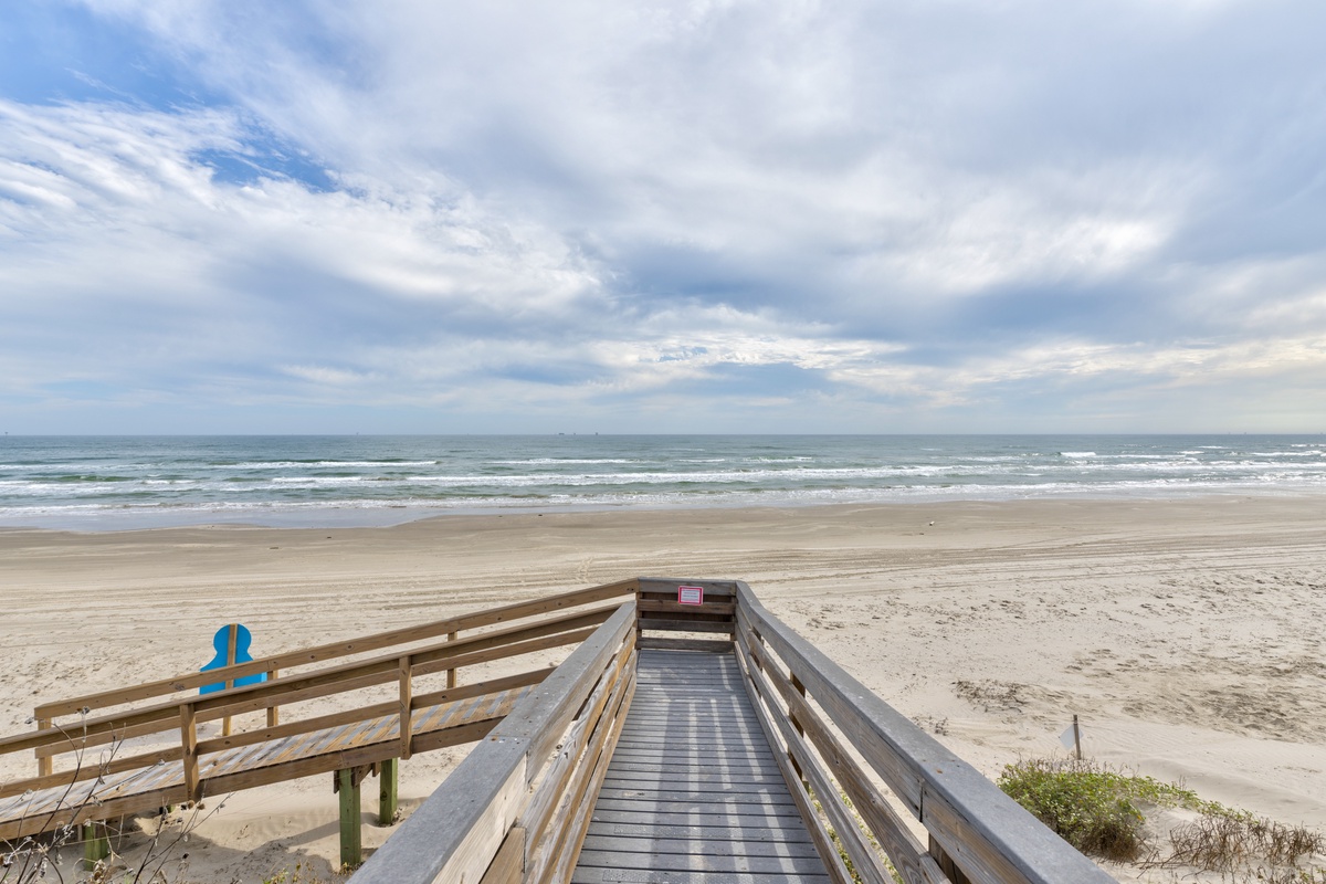 Private wooden boardwalk leads directly to pristine sandy beach with rolling ocean waves.