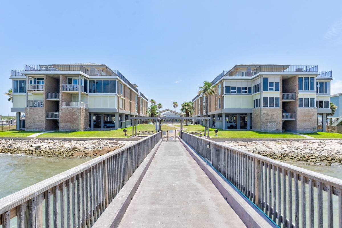 Modern waterfront property buildings connected by a private fishing pier extending into calm coastal waters.