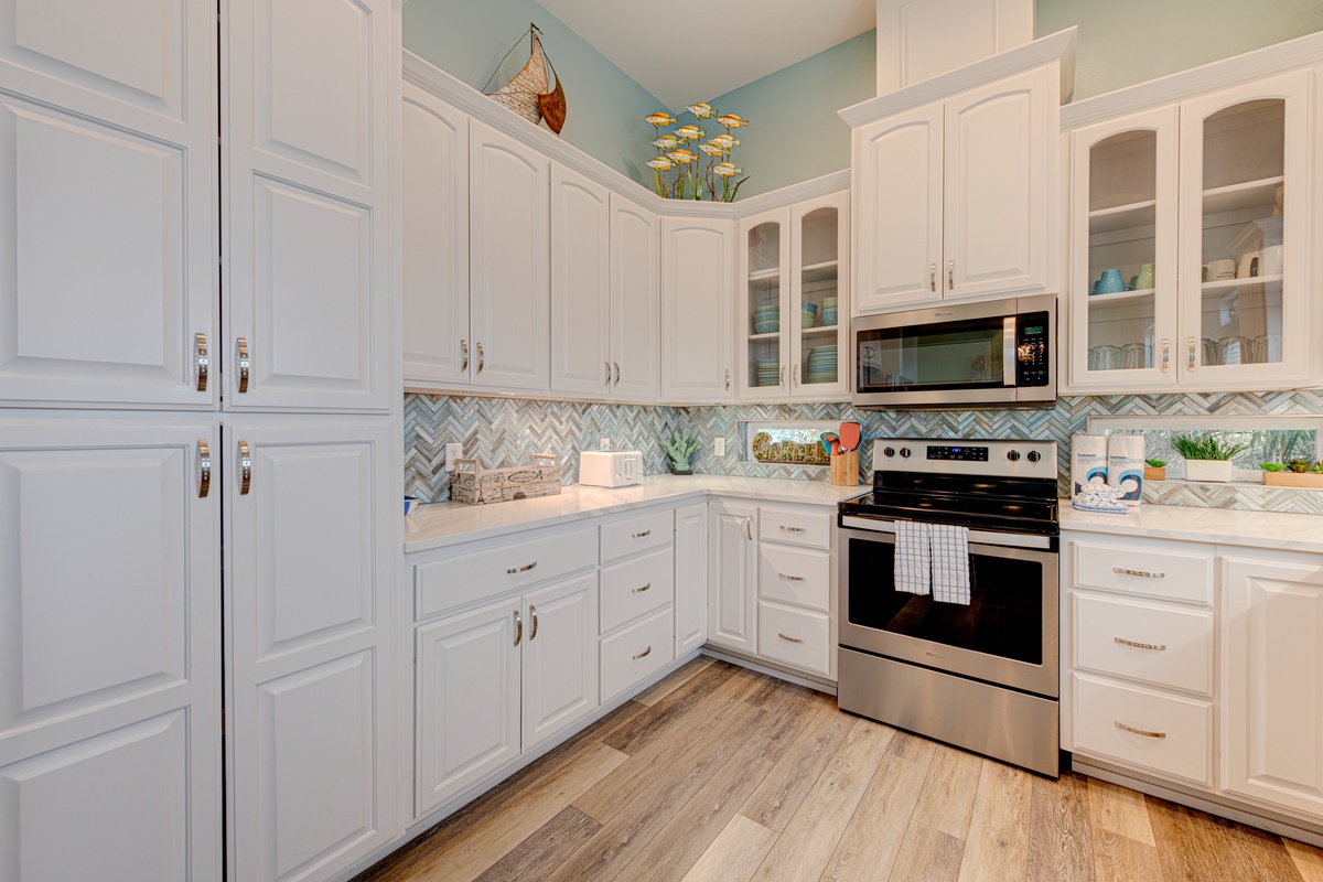 Your fully equipped kitchen features sleek white cabinetry, stainless steel appliances, and charming coastal-inspired backsplash for delightful meal preparation.