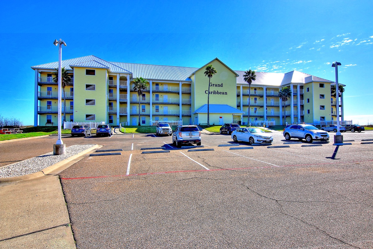 The Grand Caribbean resort features a multi-story beachfront building with convenient on-site parking and tropical palm trees throughout the grounds.