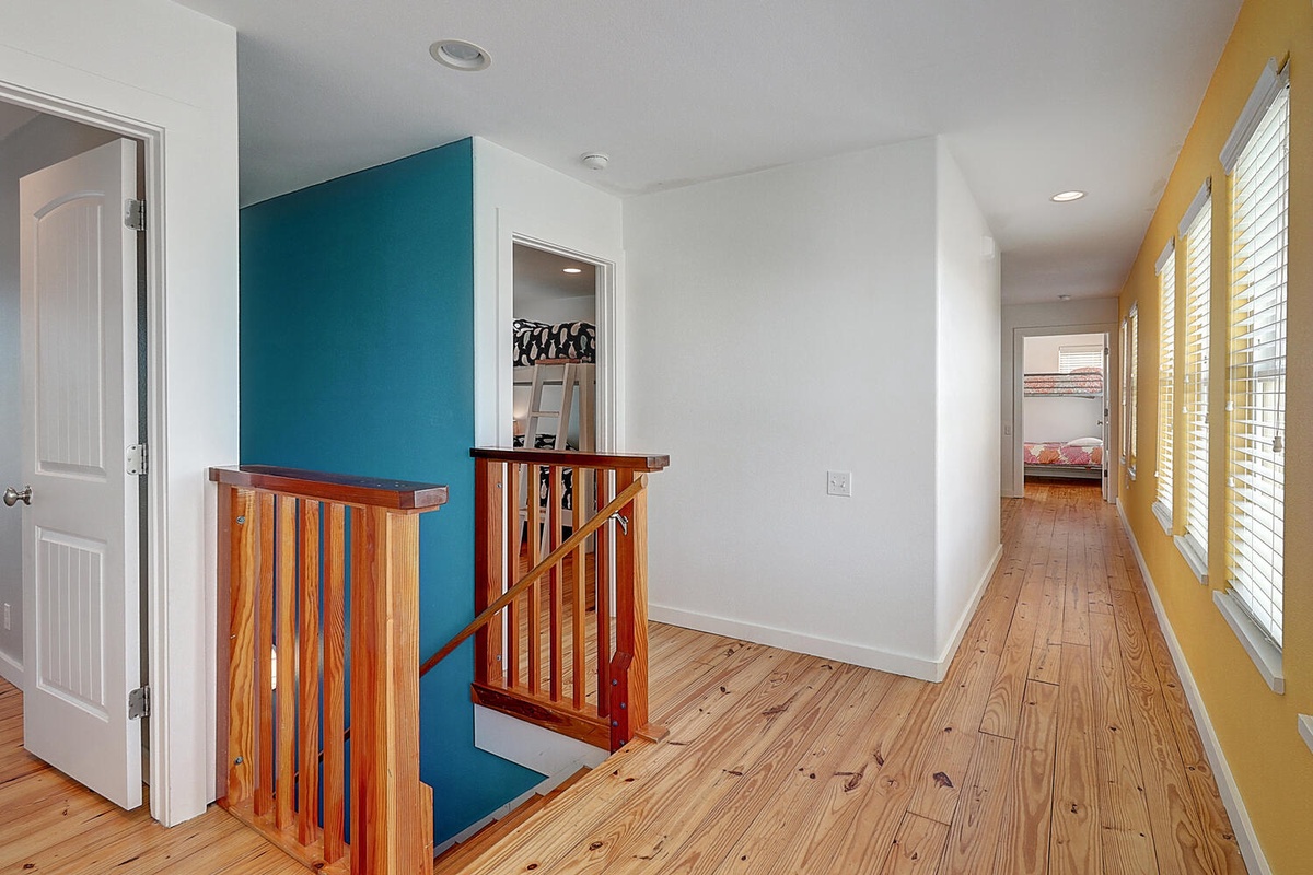 Warm hardwood floors guide you through this bright, welcoming hallway where natural light dances across colorful walls and polished railings.