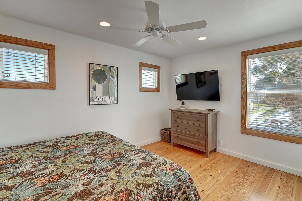 Relax in your bright bedroom with tropical-print bedding, entertainment center, and palm tree views through multiple windows.