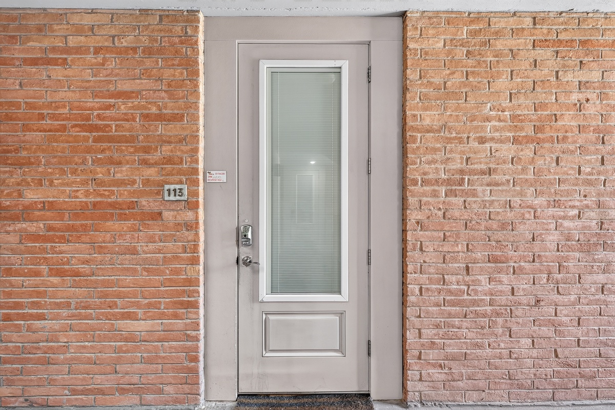 Unit 113 entrance with frosted glass door against warm brick exterior—your private retreat awaits behind this charming facade.