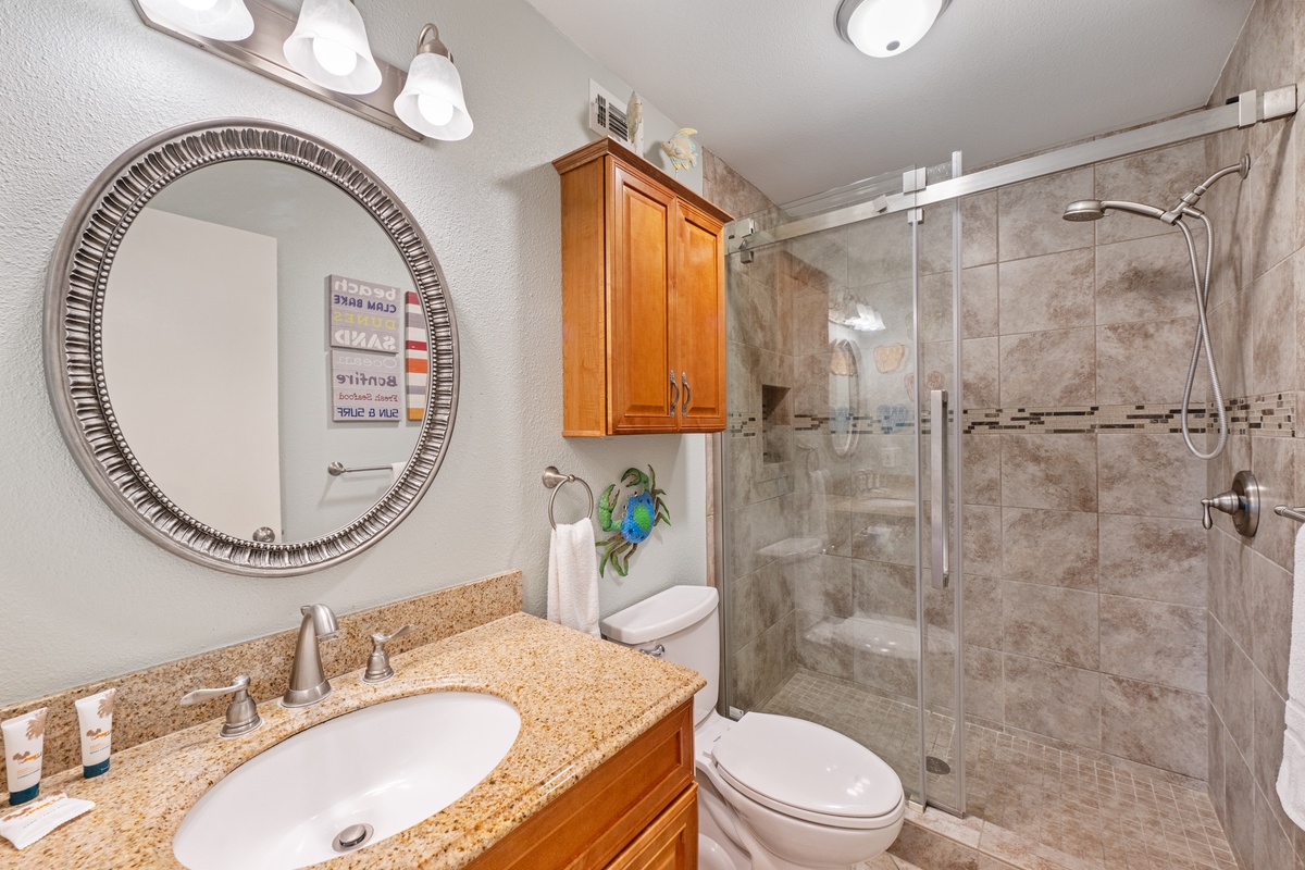 Step into your beautifully renovated bathroom featuring granite countertops, elegant tile work, and a spacious glass-enclosed shower perfect for refreshing after beach days.