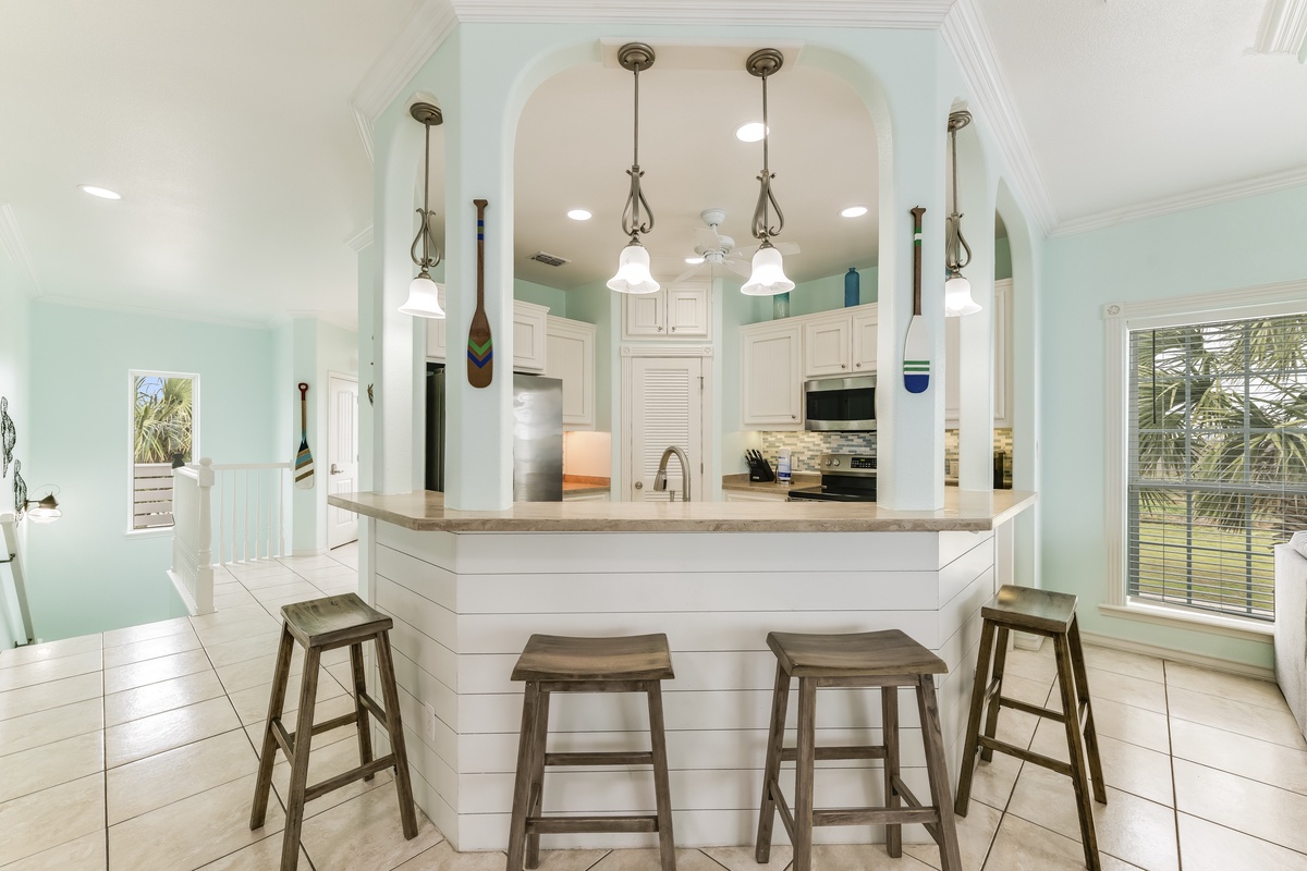 Step into your bright coastal kitchen where soothing mint walls and elegant pendant lighting create the perfect space for morning coffee or evening gatherings.