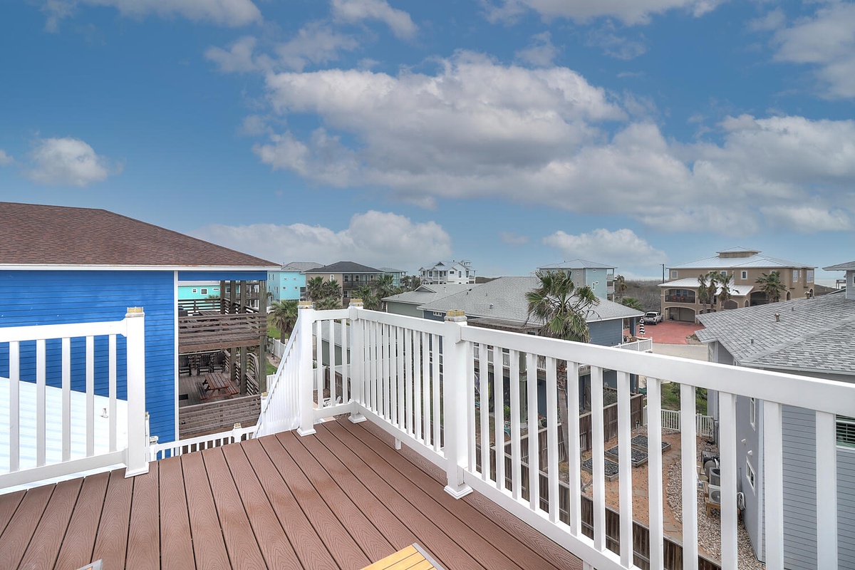 Elevated deck with white railings showcasing colorful beachside neighborhood views and blue sky backdrop.