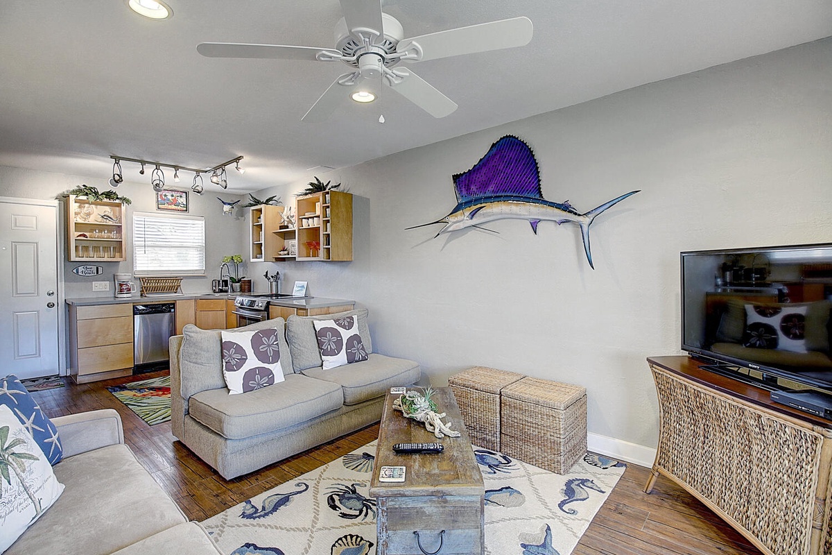Relax in your nautical-themed living space with comfortable seating, full kitchen, and tropical sailfish artwork creating a coastal vibe.