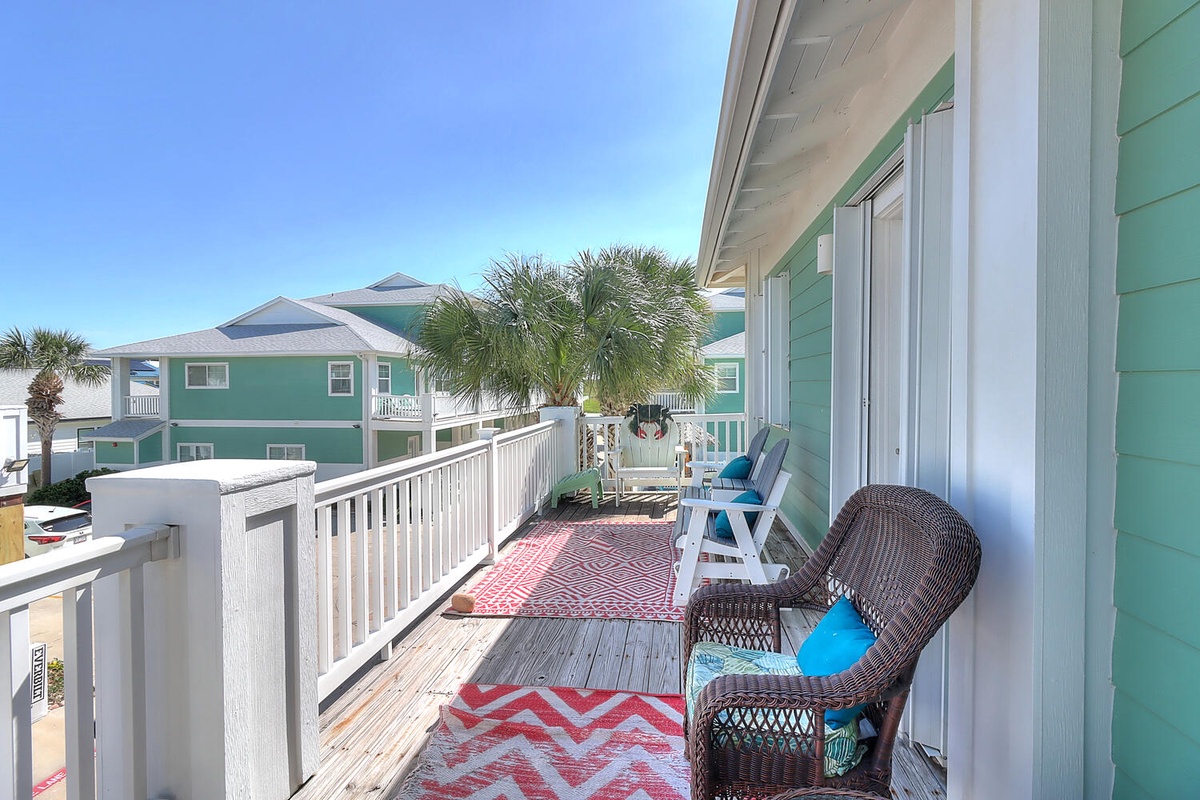 Your private balcony beckons with wicker chairs and colorful cushions, perfect for morning coffee while gazing at charming coastal homes and swaying palms.