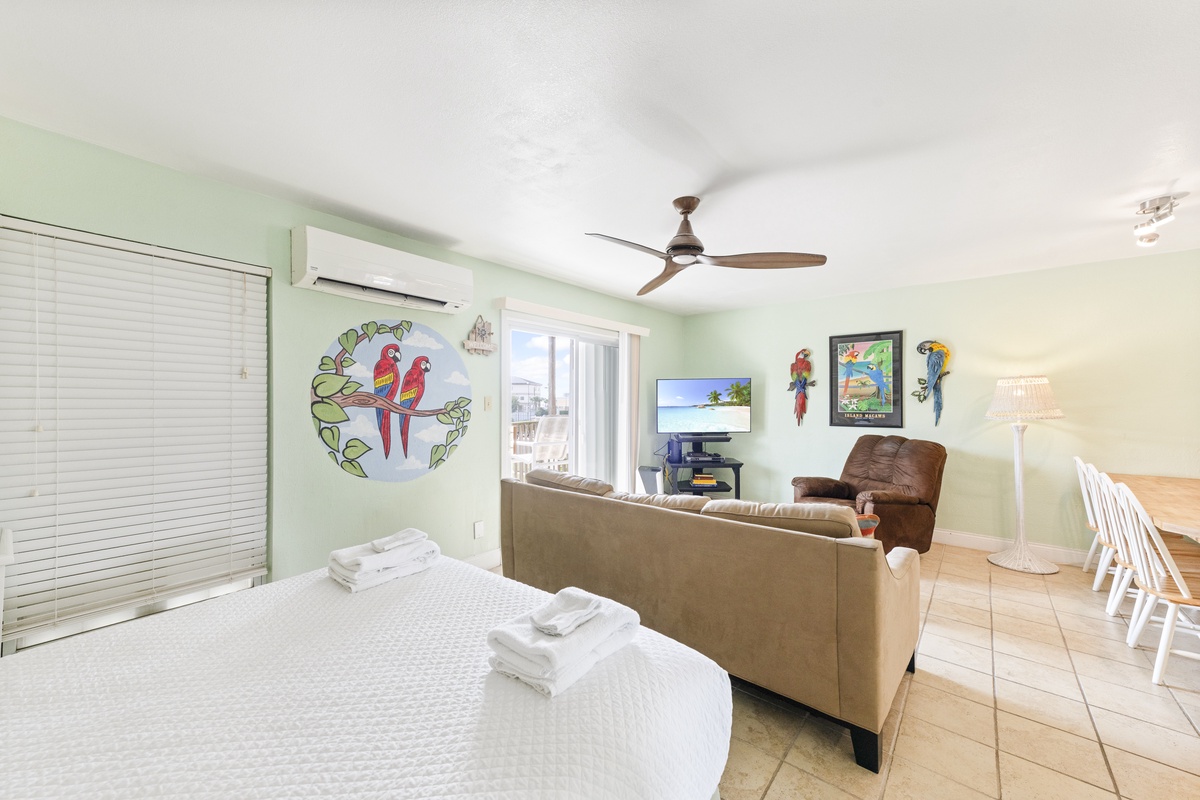 Relax in your tropical-themed living space with air conditioning, ceiling fan, and cheerful parrot artwork creating a bright, comfortable retreat.