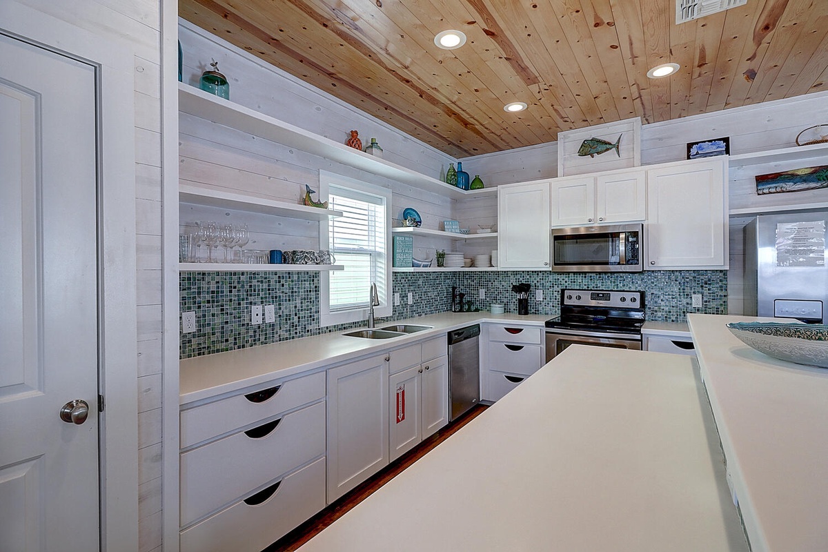 Your coastal-inspired kitchen features gleaming white countertops, turquoise tile backsplash, and warm wood ceiling—perfect for preparing seaside feasts.
