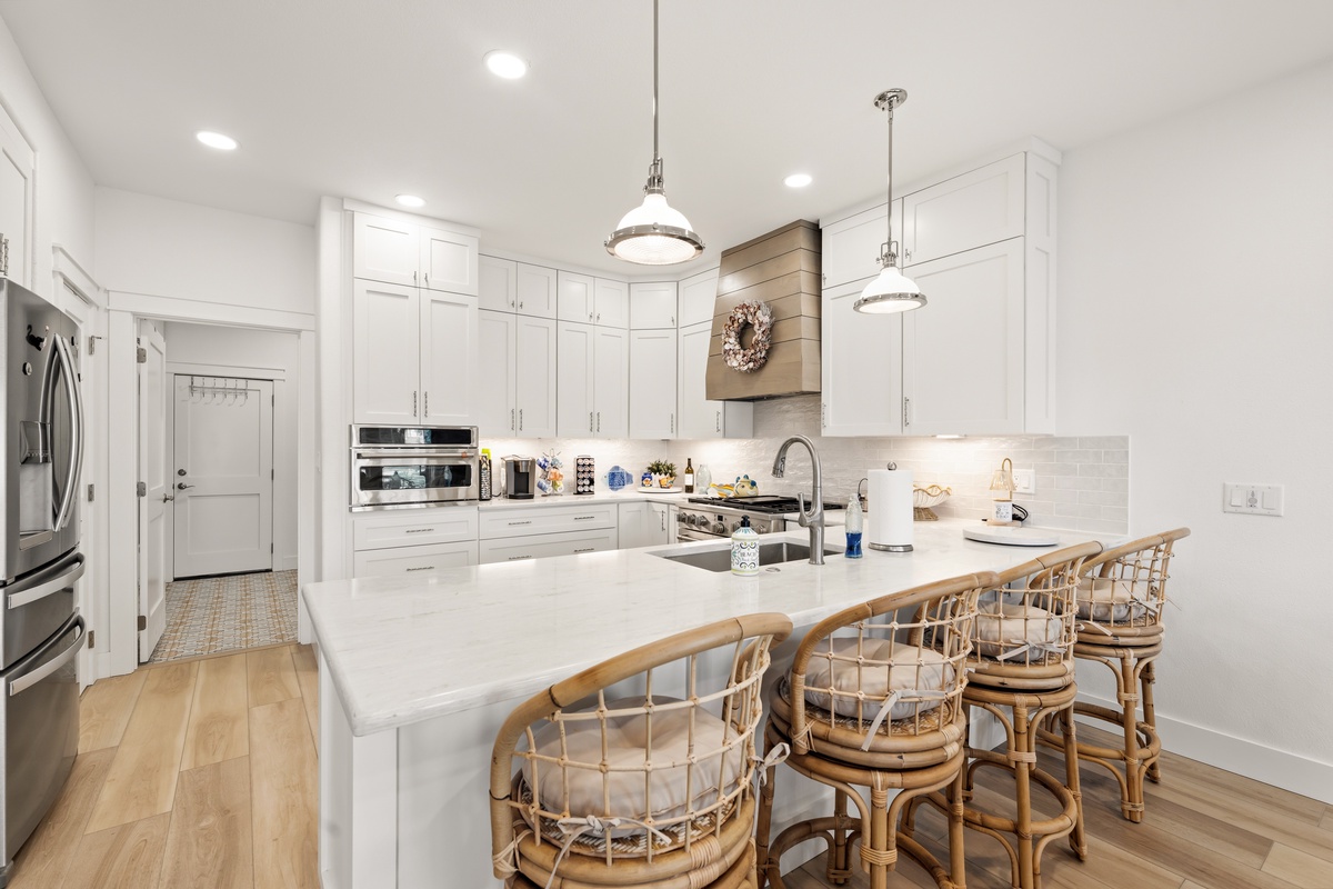 Spacious kitchen island with gleaming white countertops and coastal-style seating, flooded with natural light. Chef-ready space featuring high-end appliances and ample storage.