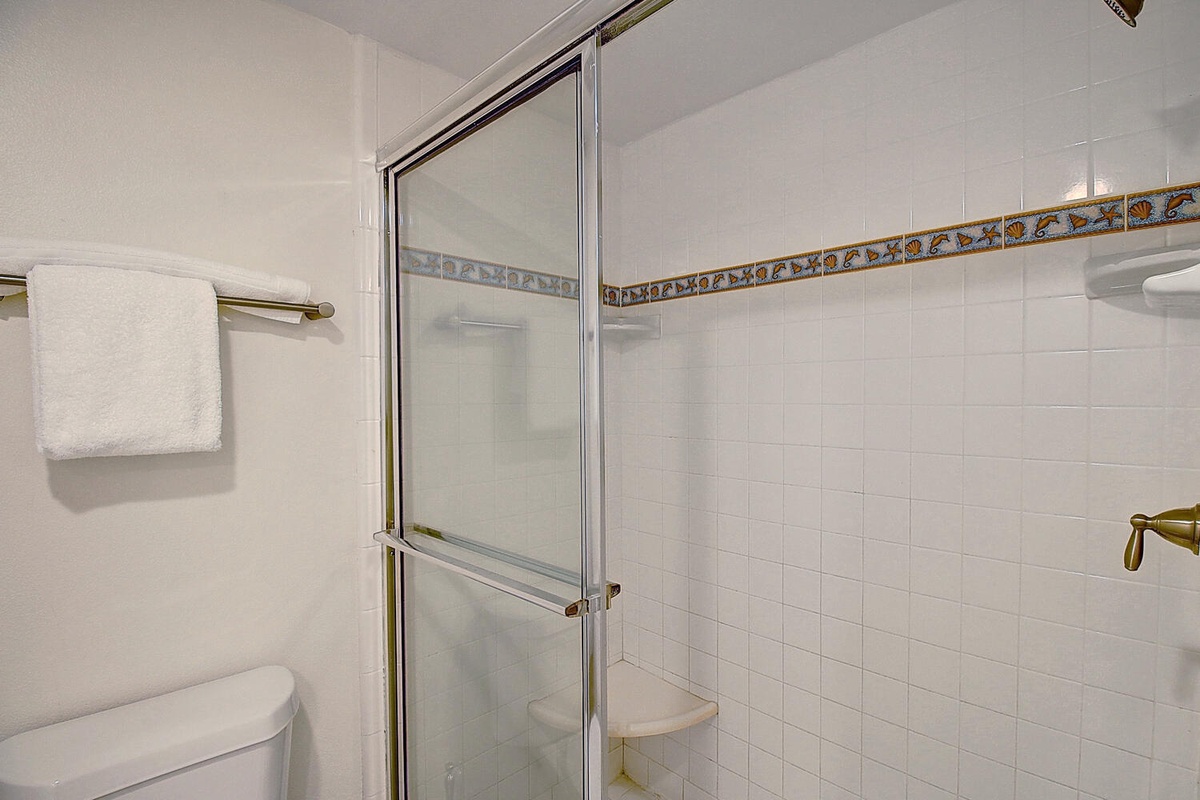 Step into your private bathroom with a spacious glass shower, classic white tiles, and fresh towels waiting for you.