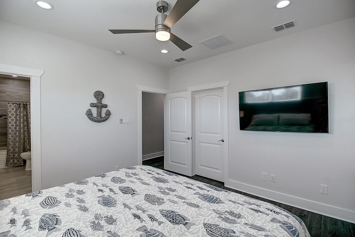 Your peaceful bedroom features a large wall-mounted TV and ceiling fan for perfect comfort after seaside adventures.
