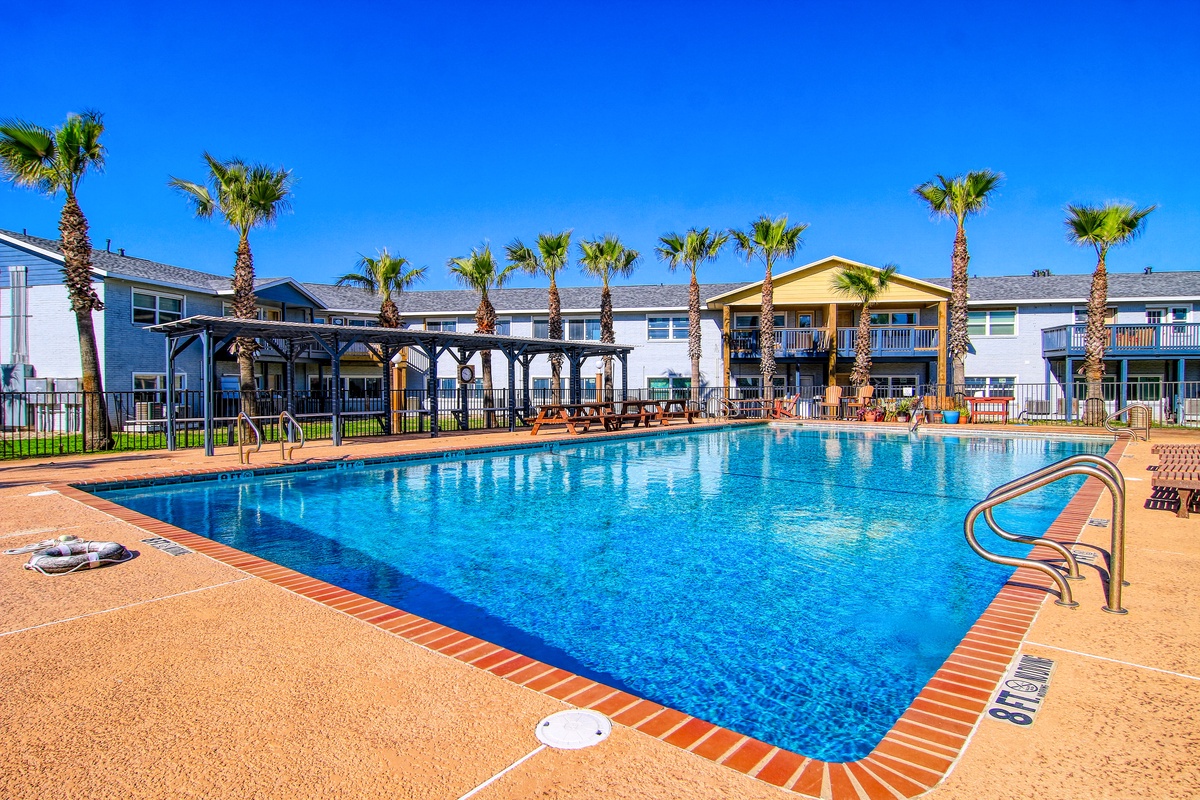 Sparkling pool area surrounded by swaying palm trees and comfortable seating under brilliant blue skies.