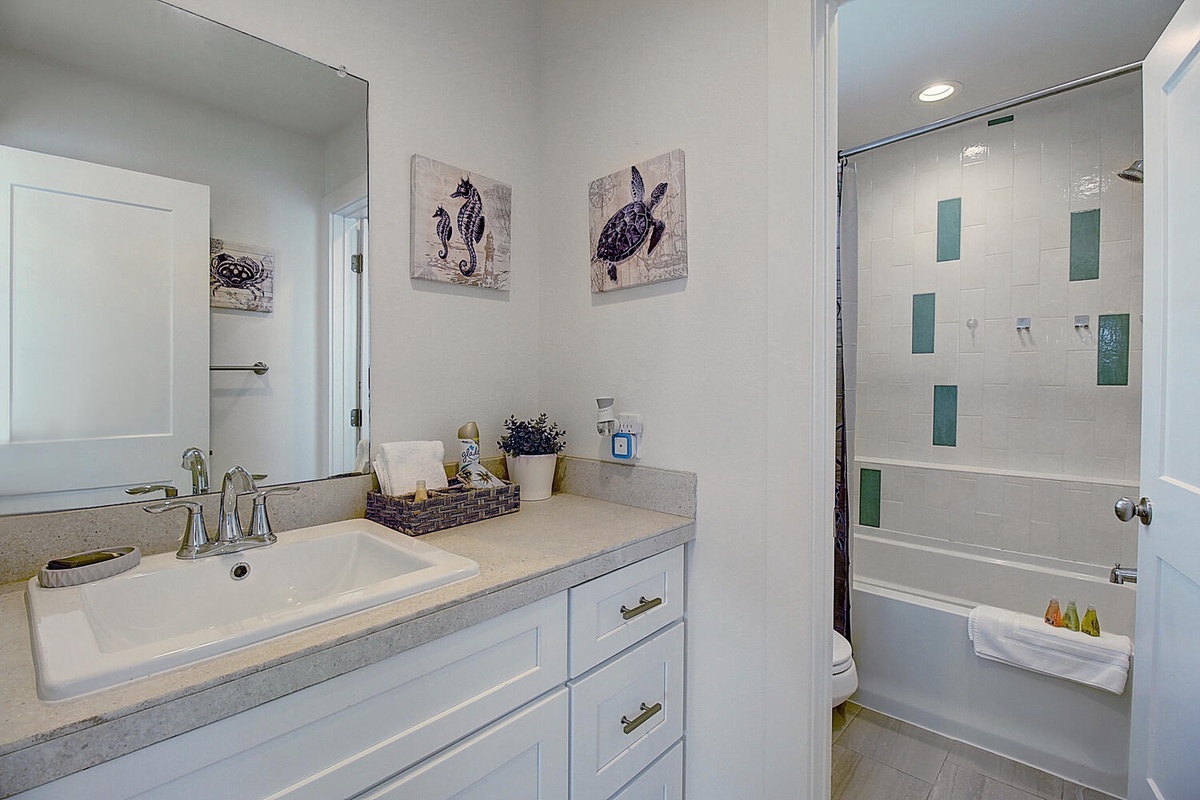 Your private bathroom features a soaking tub, spacious vanity with storage, and coastal artwork that brings beachside serenity to your daily routine.