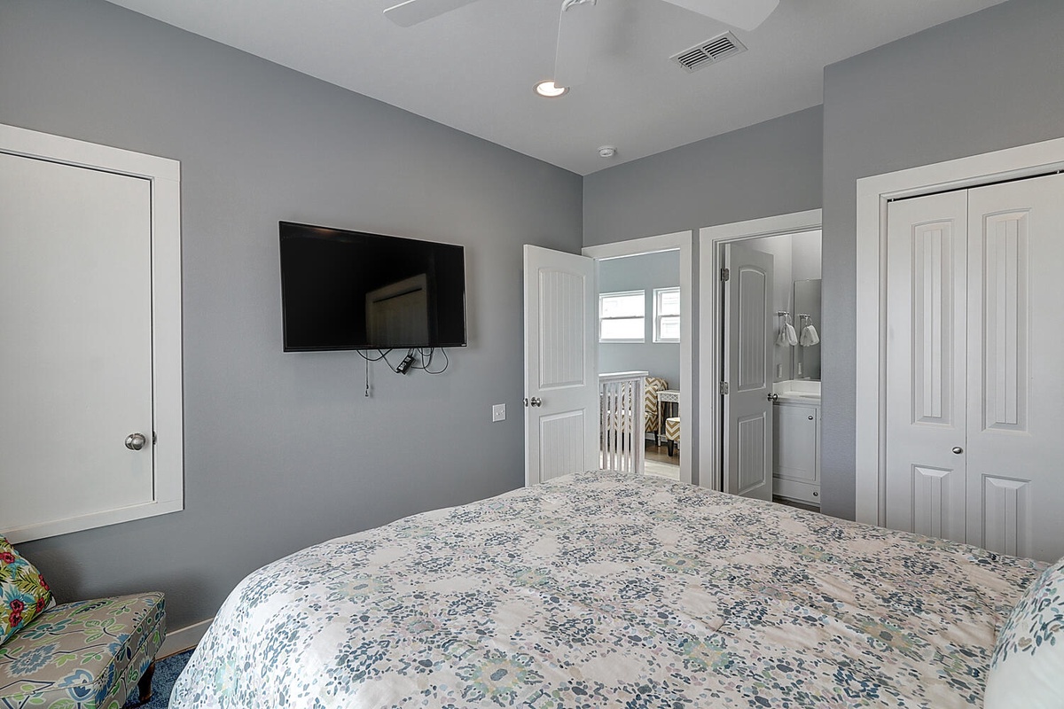Relax in your peaceful bedroom featuring soft gray walls, comfortable bedding, and modern amenities including a wall-mounted TV for cozy evenings.