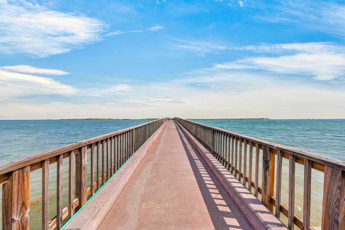 A picturesque wooden pier stretches across turquoise waters, offering a scenic pathway to explore the surrounding area. Perfect for a peaceful stroll or morning jog, with stunning coastal views in every direction.