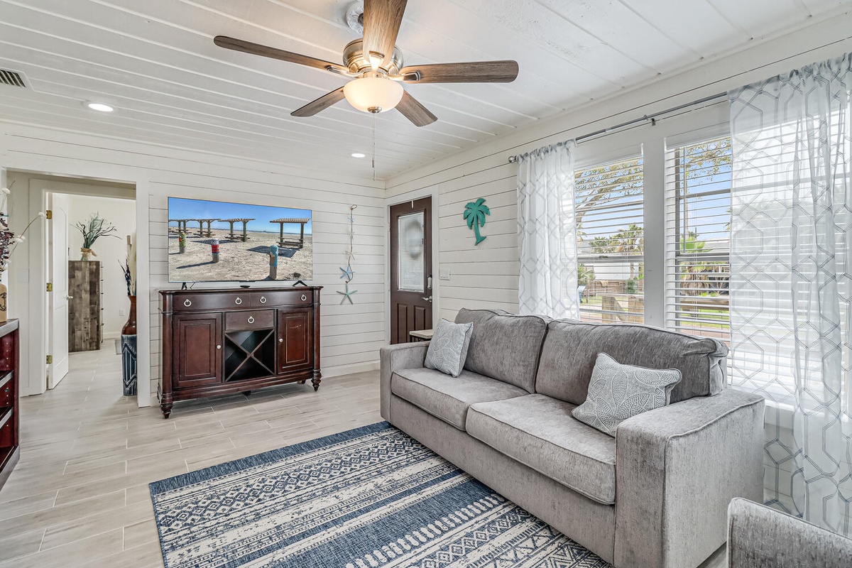 Settle into this bright living room where coastal charm meets comfort. Natural light flows through sheer curtains while you relax on the plush sofa.