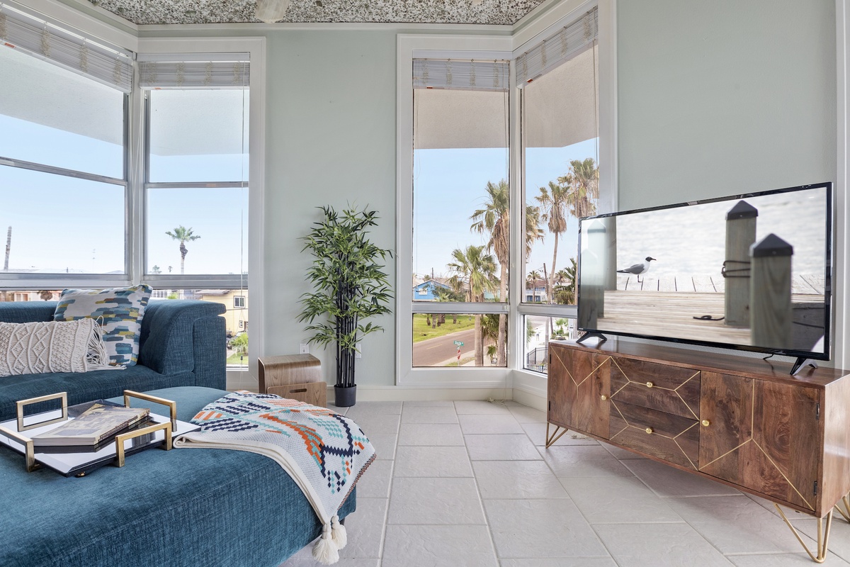 Settle into your bright living space featuring a plush teal sectional and stunning ocean views through floor-to-ceiling windows.