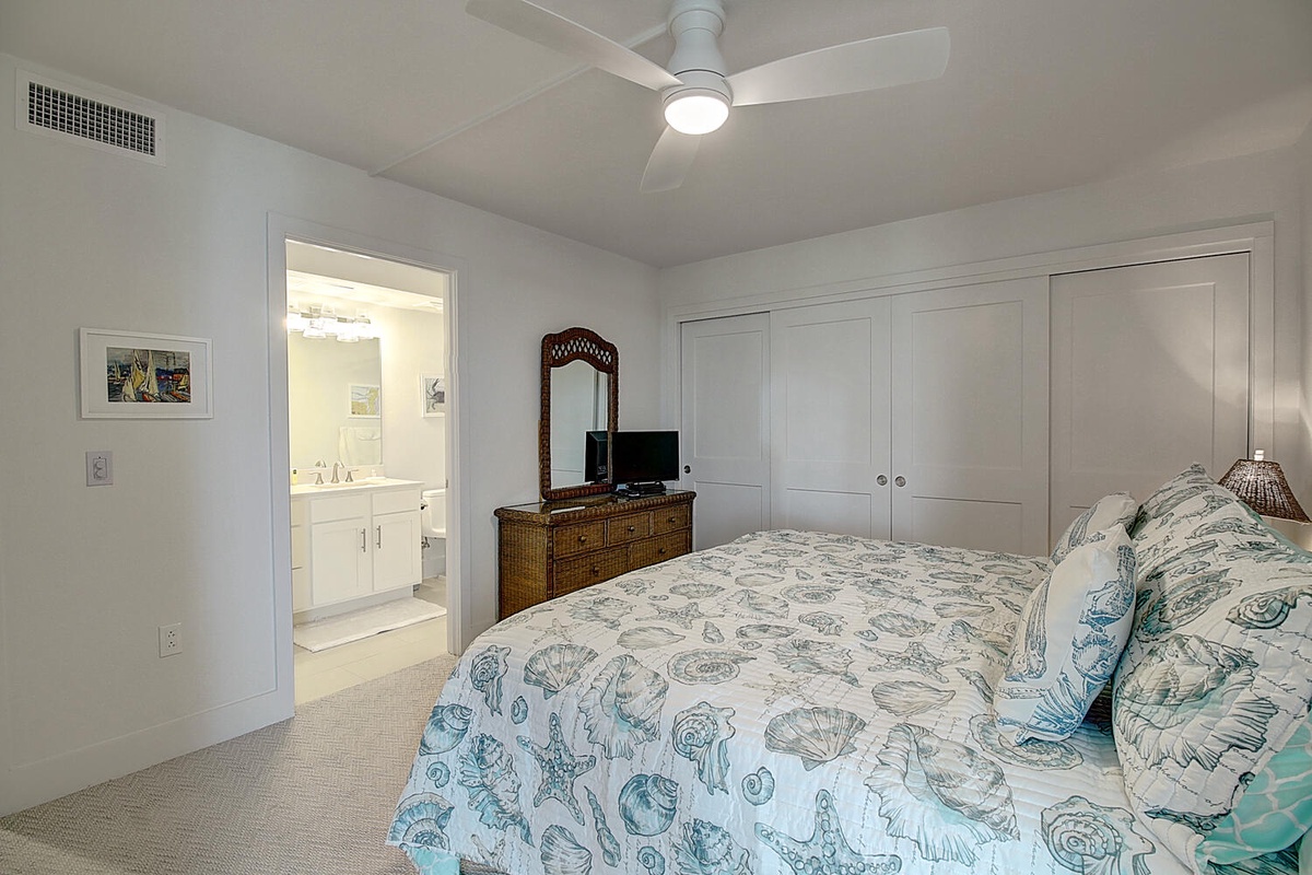 Your master suite offers coastal comfort with beautiful shell-patterned bedding, modern ceiling fan, and convenient ensuite access for relaxing nights.