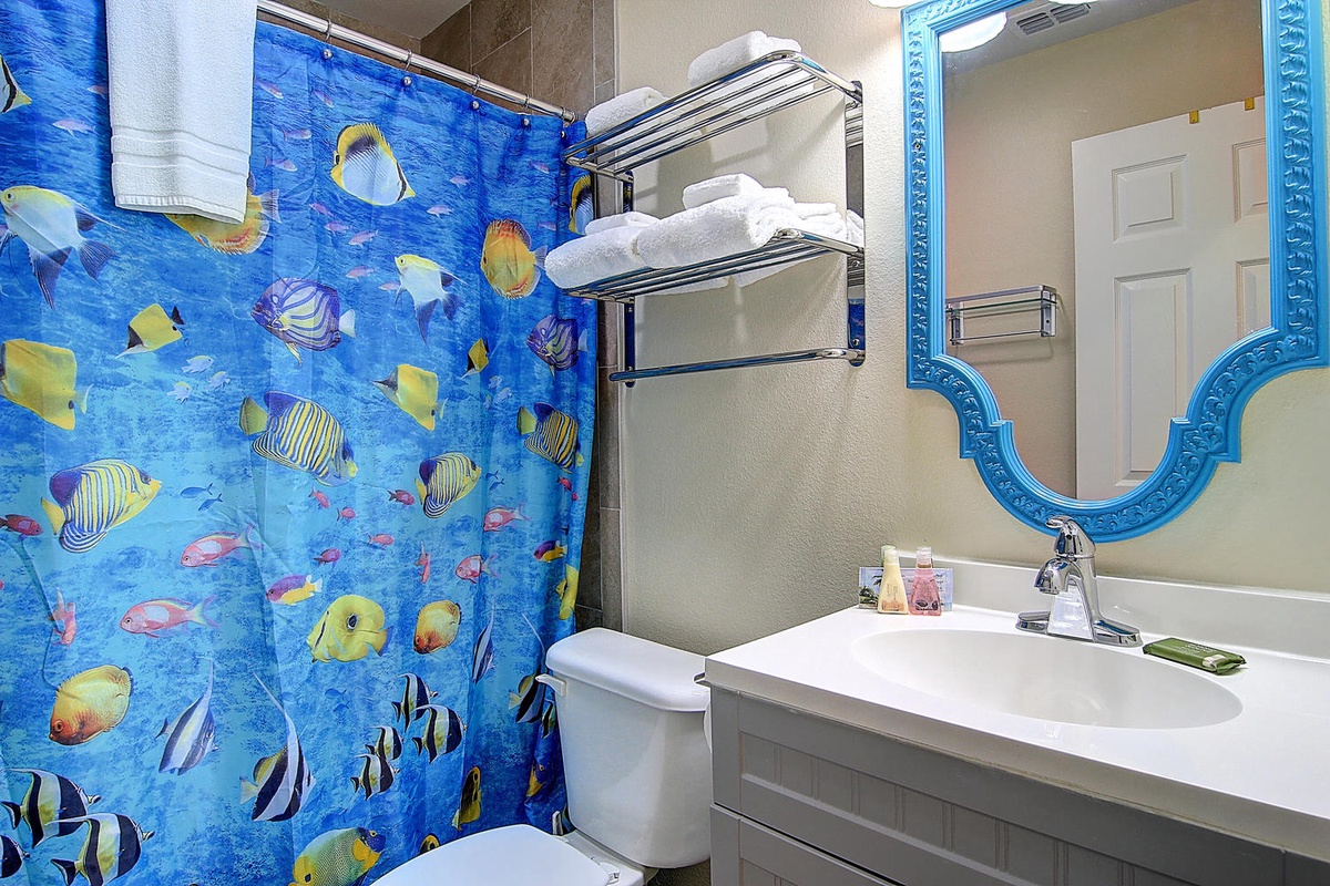 Dive into your ocean-themed bathroom featuring whimsical tropical fish curtains, fluffy towels, and a decorative mirror.