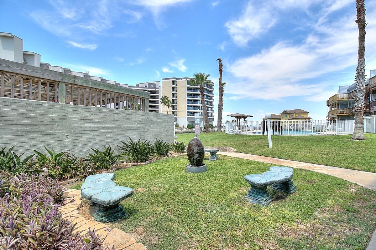 Peaceful courtyard with sculptural seating and lush greenery provides a tranquil retreat between coastal buildings.