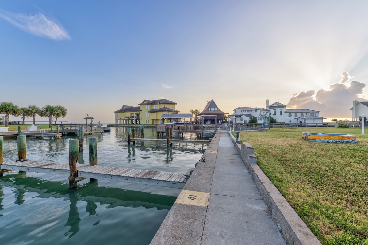 A peaceful waterfront community featuring boat docks, colorful homes, and a scenic pier stretching across calm waters beneath a dramatic sky at dusk.