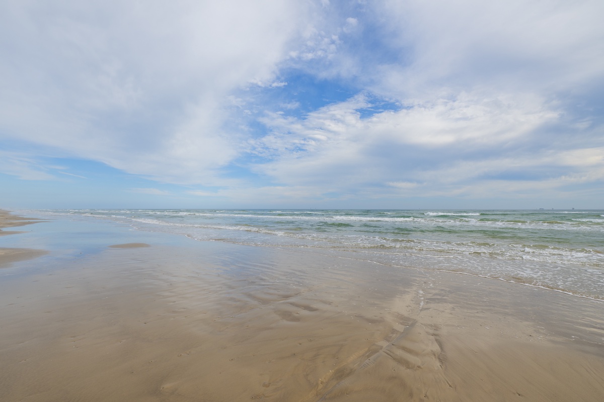 Expansive sandy shoreline meets rolling waves under a dramatic cloudy sky, creating a pristine coastal landscape.