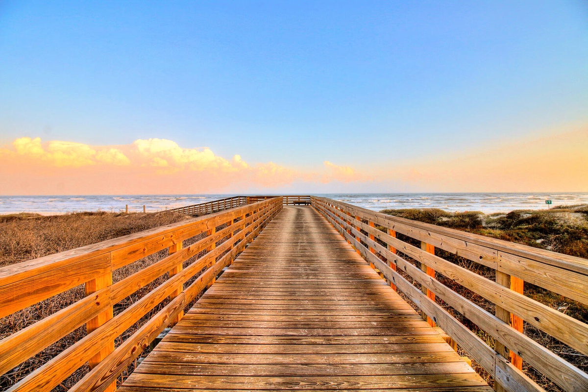 Wooden boardwalk stretches toward the ocean under a stunning sunset sky, providing scenic access to pristine coastal shores.