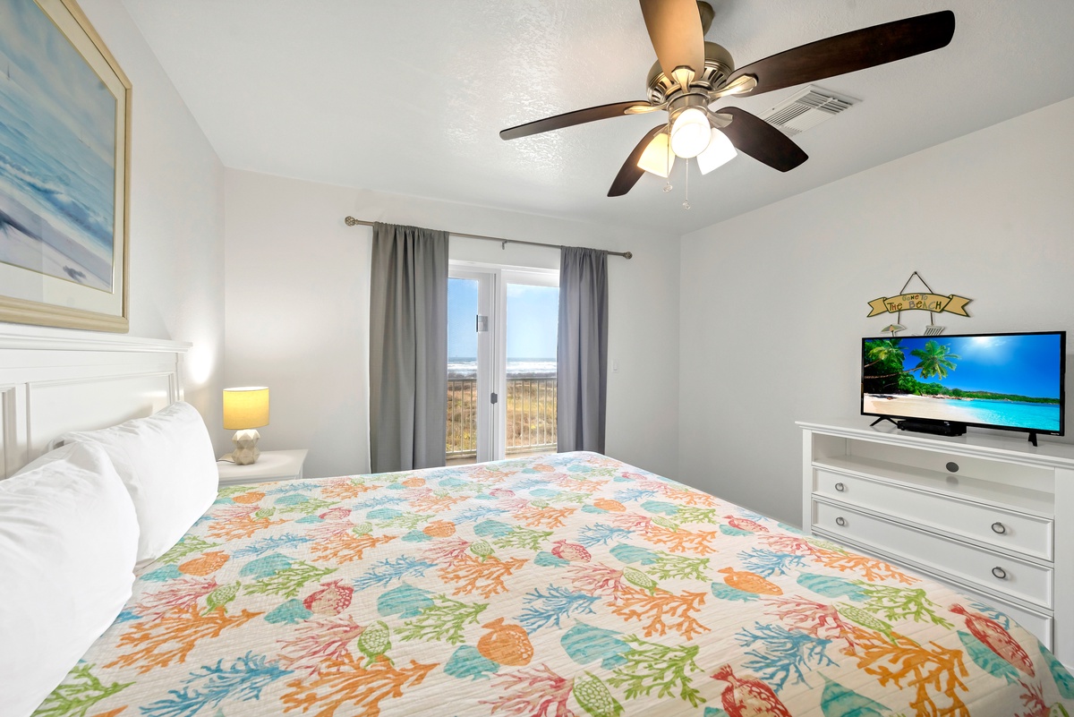 Your bright, coastal-themed bedroom features a comfy bed and cheerful decor, keeping you cool with a ceiling fan. Step through the glass doors to soak in the sunny surroundings beyond.
